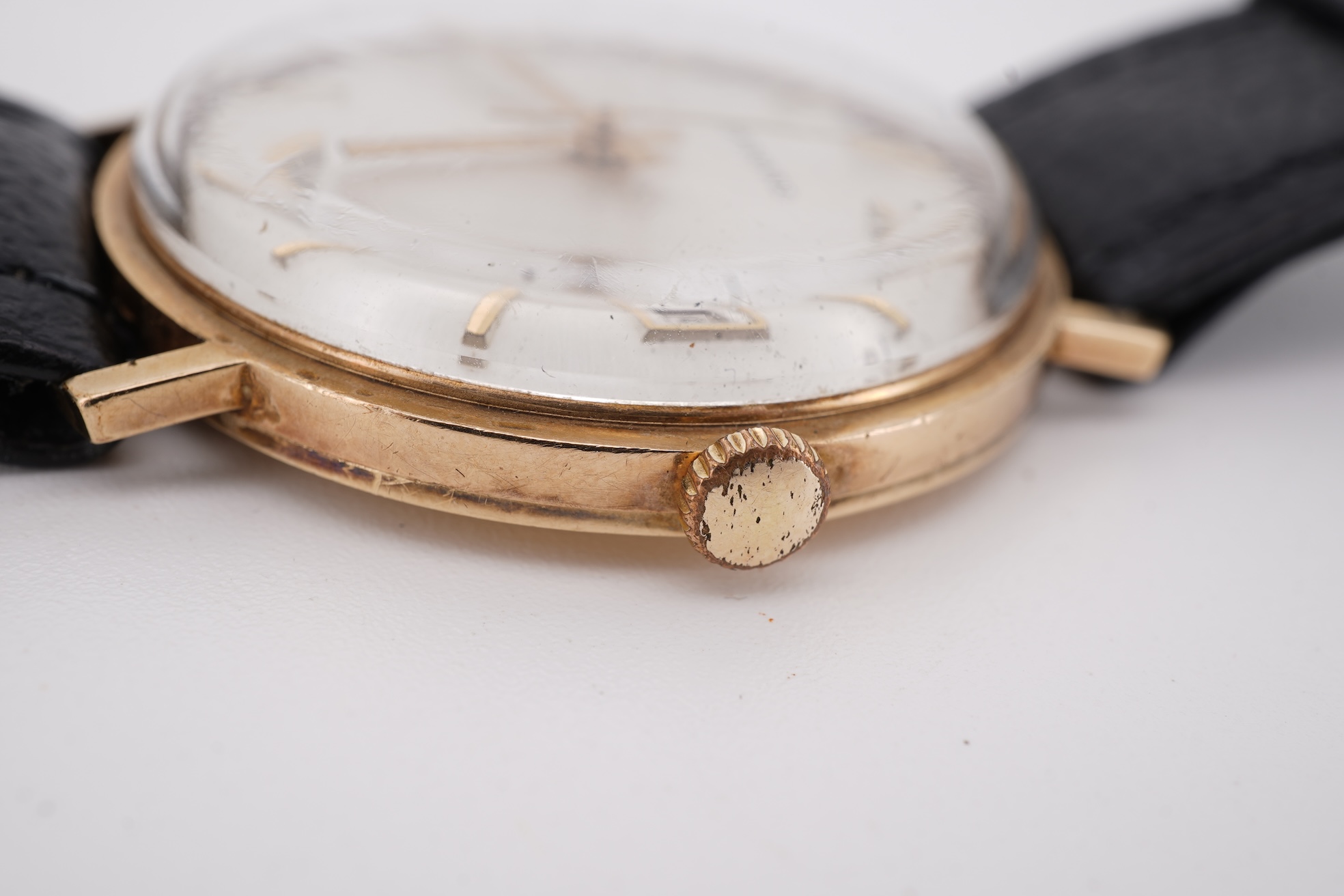 A gentleman's yellow metal Garrard manual wind wrist watch, with baton numerals and date aperture, case diameter 34mm, on a black leather strap.